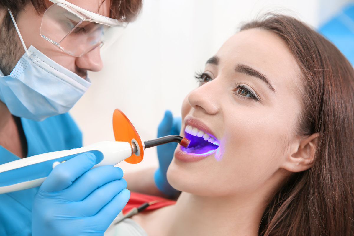 Dentist doing procedure with dental curing UV light in clinic Dentist doing procedure with dental curing UV light in clinic